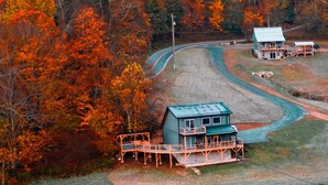 Une maison avec un toit bleu et une terrasse, entourée d’une forêt aux couleurs automnales.