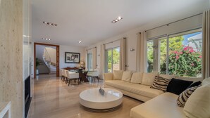 A spacious living room with a large round coffee table, a beige sofa, and a dining area with a glass table and chairs. - Magnificent villa a few steps from Playa de Muro (Alcúdia)
