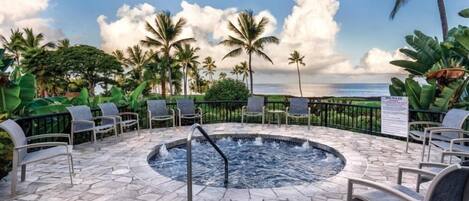 A stone-tiled outdoor area with a hot tub, lounge chairs, and a view of the ocean.