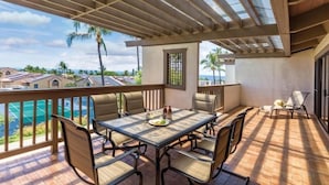 Eine überdachte Terrasse im Freien mit Tisch und Stühlen, mit Blick auf einen Pool und Wohnhäuser.