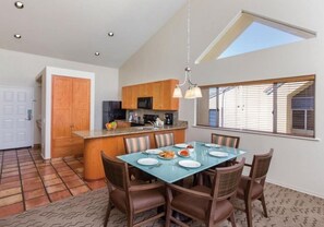 Una cocina moderna con armarios de madera, una isla central y una zona de comedor con una mesa de vidrio y sillas marrones.