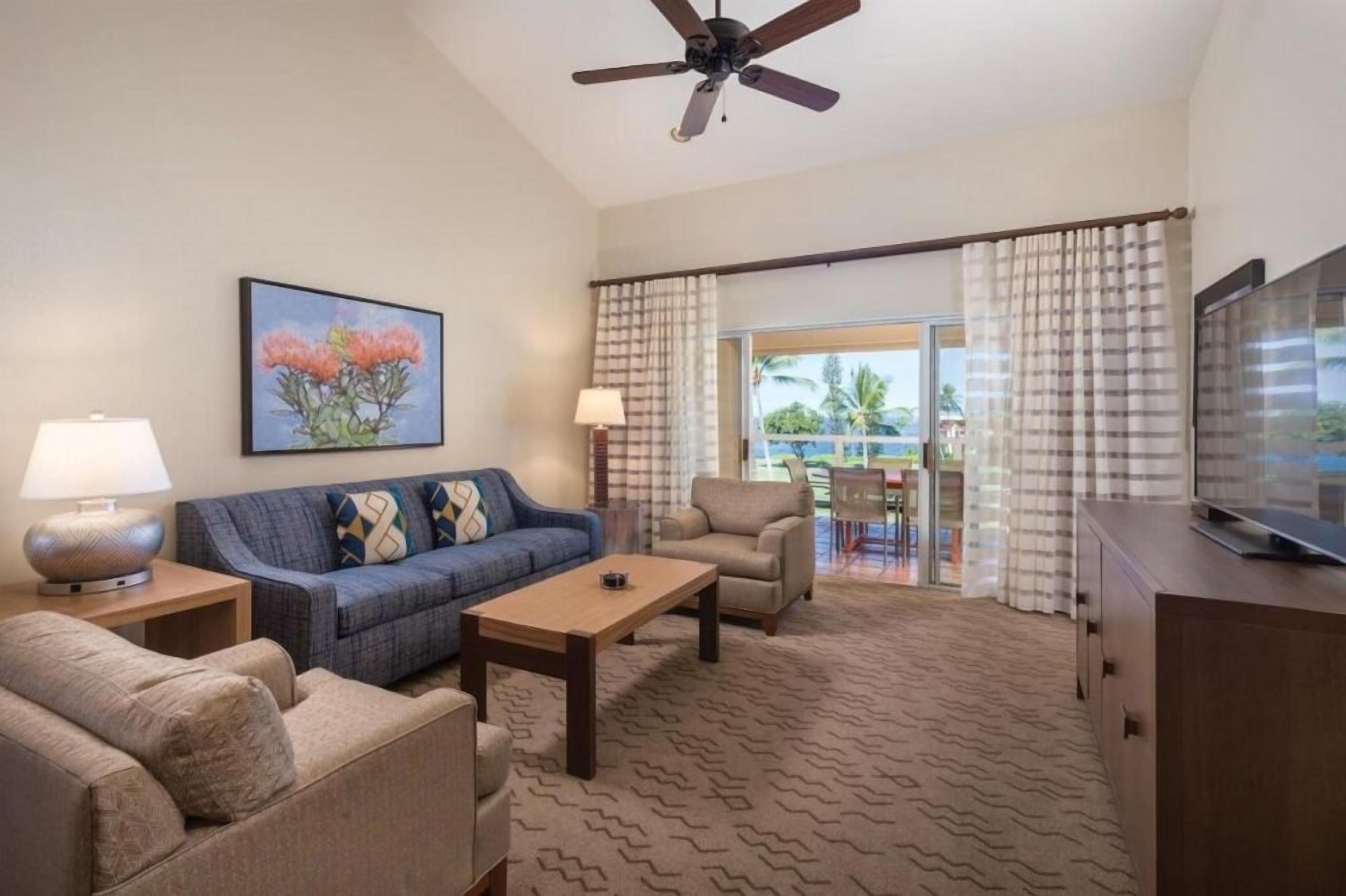 A hotel room with a sofa, armchair, coffee table, TV, and a painting on the wall.