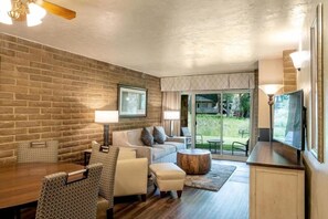 A modern living room with a brick wall, a sofa, a coffee table, and a TV. - Weekend Getaway 2BR Condo with Balcony & Jacuzzi (Vail)