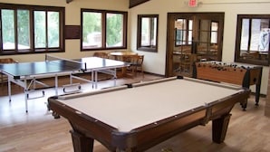 A billiards room with a pool table, foosball table, and ping pong table.