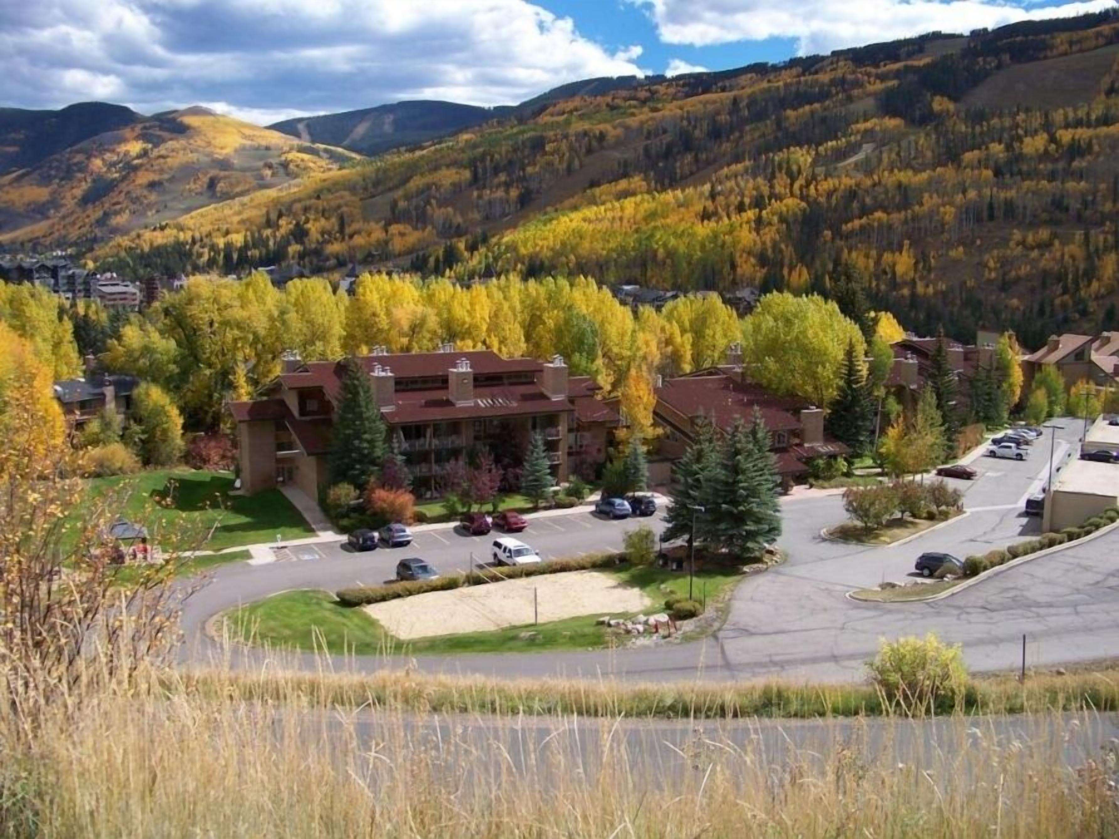 Un hotel a più piani con un parcheggio e vista sulle montagne circostanti e il fogliame autunnale.