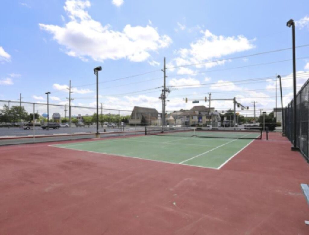 Ein Tennisplatz mit roter Belag und einer grünen Spielfläche, umgeben von einem Zaun und Laternen.