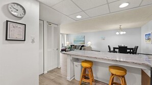 A modern kitchen with a granite countertop, two wooden stools, a clock, and a welcome sign on the wall. - ⭐️Quay 2005 Amazing Bay/Ocean Views In/Outdoor Pools⭐️ (Ocean City)