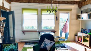 A cozy room with a wooden ceiling, a green armchair with a deer pillow, a blue sofa, a small table, and a bookshelf. - Studio with kitchen, fireplace, terrace, barbecue - dogs allowed - Hohes Venn - Eifel (Monschau)