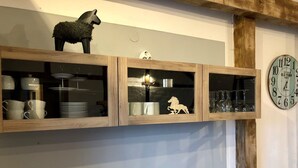 A shelf with glass-fronted cabinets containing kitchenware, a decorative horse figure, and a clock on the wall. - Studio with kitchen, fireplace, terrace, barbecue - dogs allowed - Hohes Venn - Eifel (Monschau)