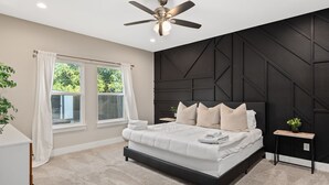 A bedroom with a bed, a ceiling fan, a window with curtains, and a wall with geometric patterns. - Luxury Comfort 5 Bedroom Home in Heart of Dallas (Dallas)
