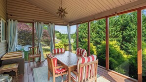 Une terrasse couverte avec une table en bois et des chaises à rayures, de grandes fenêtres et un luminaire en forme d’étoile.