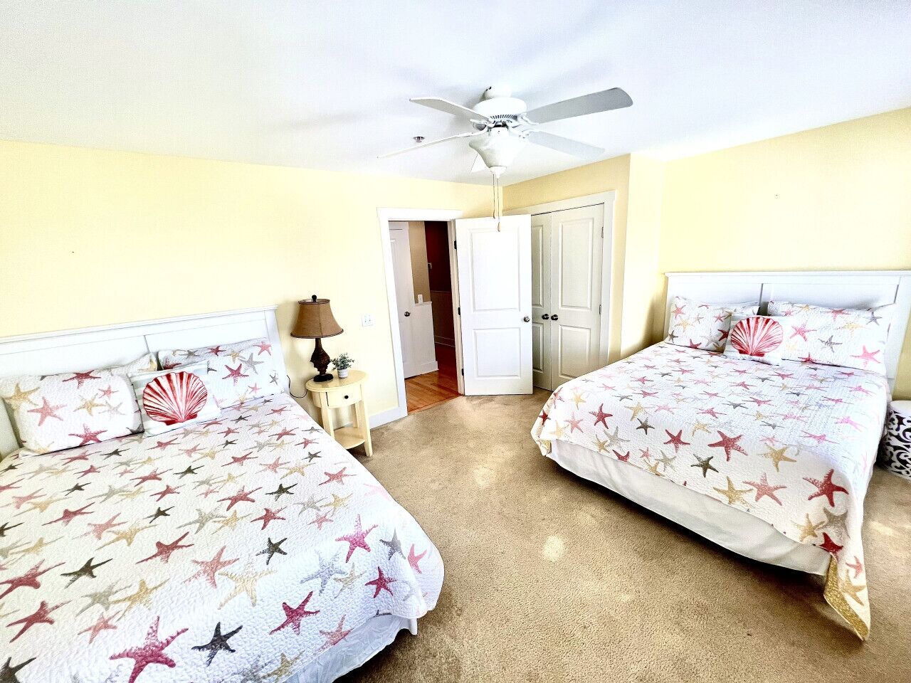 A hotel room with two beds, a ceiling fan, a nightstand, and a door leading to another room.