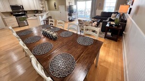A spacious living area with a dining table set with placemats, a kitchen with modern appliances, and a balcony with a view. - Tybee Retreat Unit 3 (Tybee Island)