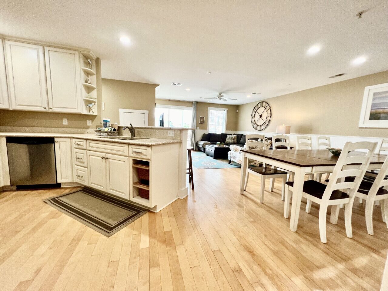 A spacious kitchen with white cabinets, a wooden dining table, and a large clock on the wall.