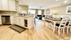 A spacious kitchen with white cabinets, a wooden dining table, and a large clock on the wall. - Tybee Retreat Unit 3 (Tybee Island)