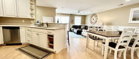 A spacious kitchen with white cabinets, a wooden dining table, and a large clock on the wall.