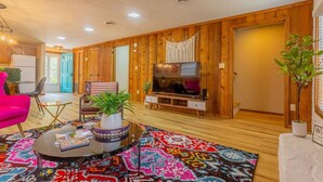 A modern living room with a wooden interior, a television, a coffee table with books, and a colorful rug. - ACID WASH @ DOLLYS DRIVE * Wifi Grill Woods Mtns (Sevierville)