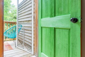 Eine grüne Tür mit schwarzem Griff, ein Holzterrasse und ein türkisfarbener Stuhl.