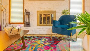 A cozy living room with a stone fireplace, a blue armchair, a colorful rug, and a wooden coffee table. - PSYCHEDELIC @ DOLLYS DRIVE * Wifi Grill Woods Mtns (Sevierville)