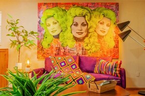Ein Zimmer mit einem violetten Sofa, einer bunten Decke und einem Wandteppich mit grünen Haaren.