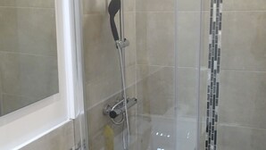 Ein modernes Badezimmer mit einer Glaskabine zur Dusche, einem weißen Waschbecken und einem Spiegel.