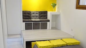 Ein gemütliches Schlafzimmer mit Bett, einer kleinen Sitzecke mit Kissen und einem Fenster.