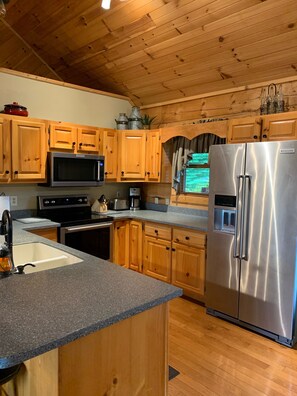 A kitchen with wooden cabinets, a stainless steel refrigerator, a microwave, and a sink.