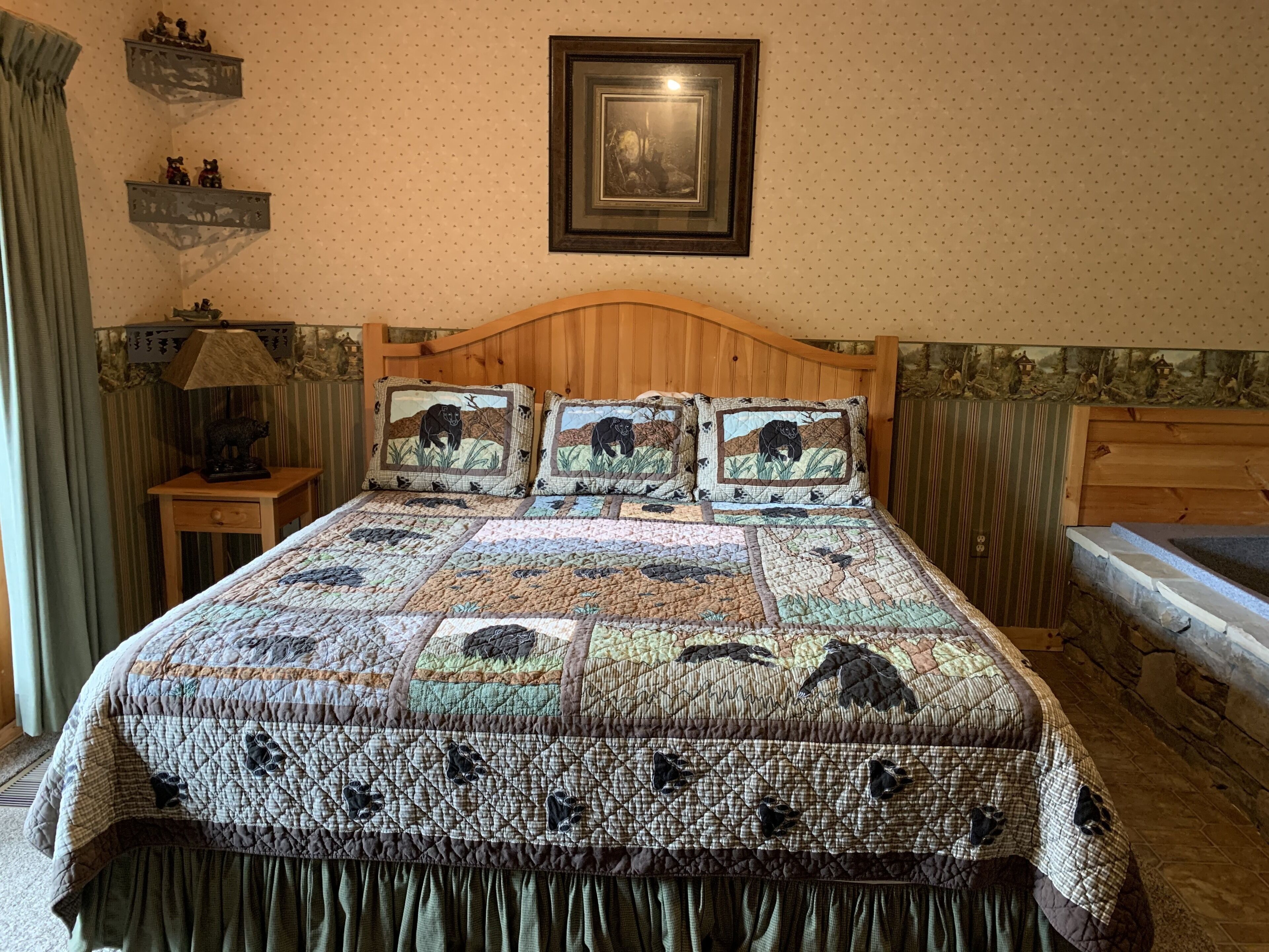Una cama con una colcha acolchada de estampados de animales, un cabecero de madera, una mesita de noche con una lámpara y un cuadro en la pared.