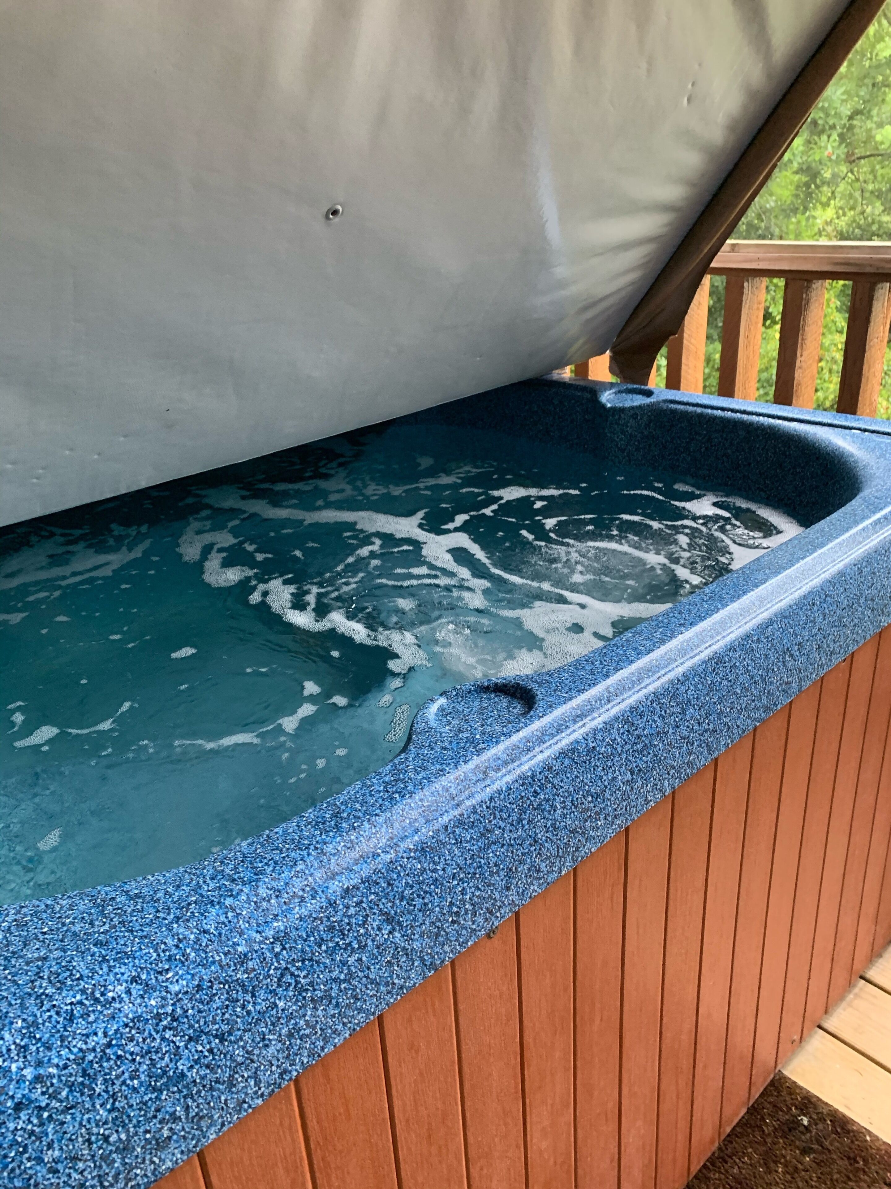 A hot tub with a blue textured exterior, wooden deck, and a metal roof structure.