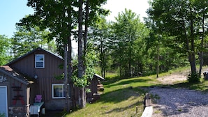 A rustic cabin with a porch, a small shed, and a gravel driveway.