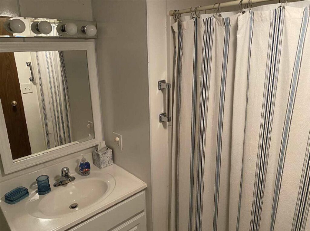 Een badkamer met een wit wastafelmeubel, spiegel en een badgordijn met strepen.