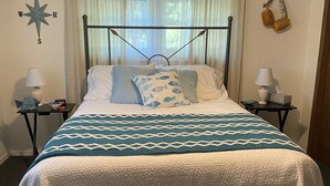 Un lit bien fait, recouvert d’une couvre-lit à motifs blancs et bleus, avec une tête de lit en métal et deux tables de chevet sur lesquelles sont posées des lampes et une horloge.