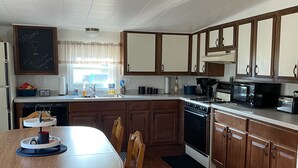 Une cuisine avec des meubles de rangement en bois, une table à manger avec des chaises, une cuisinière, un four à micro-ondes et un panneau d’affichage noir.