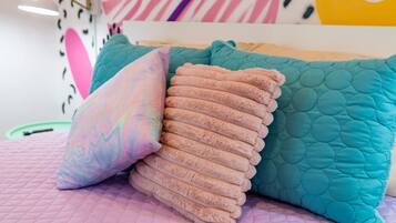 A bed with teal and pink pillows, a pink quilted bedspread, and a wall with abstract art.