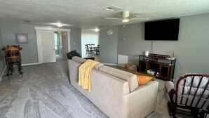 A living room with a grey sofa, a wooden chair, a flat-screen TV, and a dining area in the background. - Quiet area and canoeing steps away from the front door. (Port Richey)