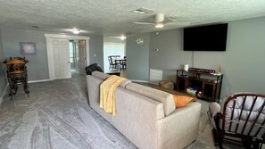 A living room with a grey sofa, a wooden chair, a flat-screen TV, and a dining area in the background. - Quiet area and canoeing steps away from the front door. (Port Richey)