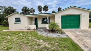 A single-story house with a green garage door, a small porch with a white railing, and a number '5229' on the front wall. - Quiet area and canoeing steps away from the front door. (Port Richey)