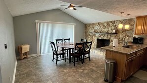 A kitchen with a stone wall, a fireplace, a dining table with chairs, and a ceiling fan. - Quiet area and canoeing steps away from the front door. (Port Richey)