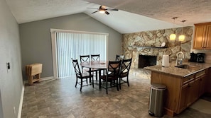 A kitchen with a stone wall, a fireplace, a dining table with chairs, and a ceiling fan. - Quiet area and canoeing steps away from the front door. (Port Richey)