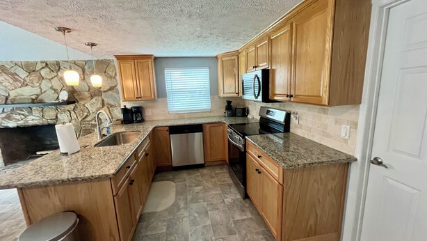 A compact kitchen with granite countertops, wooden cabinets, a dishwasher, a stove, and a microwave. - Quiet area and canoeing steps away from the front door. (Port Richey)