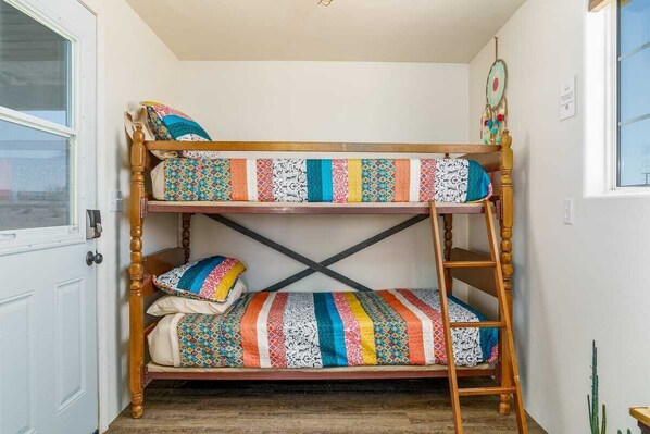 A bunk bed with colorful bedding in a small room with a window and a door.