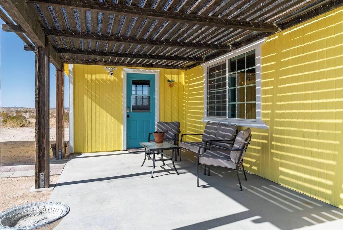 A covered patio with a yellow exterior wall, a blue door, and a window.