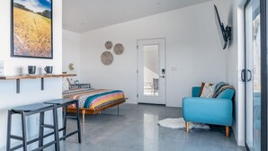 A modern bedroom with a bed, a blue sofa, a desk, and a large window. - ❤Hot Tub + Close to Downtown JT ❤ Fully Fenced + Firepit Mini❤ (Joshua Tree)