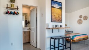 A modern bedroom with a bed, a desk, and a chair. There is a door leading to a bathroom and a kitchen. - ❤Hot Tub + Close to Downtown JT ❤ Fully Fenced + Firepit Mini❤ (Joshua Tree)