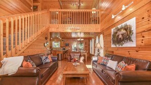 Interior espacioso de una cabaña de madera, con una zona de estar central que incluye dos sofás, una mesa de centro y una escalera que conduce a un nivel superior.