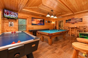 A wooden interior with a pool table, foosball table, and a television displaying a sports game. - ❤Family Friendly❤3 Min to Parkway❤Gameroom, Hot Tub, Theater❤ (Pigeon Forge)