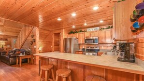 Interior de una cabaña de madera con cocina, comedor y una escalera.