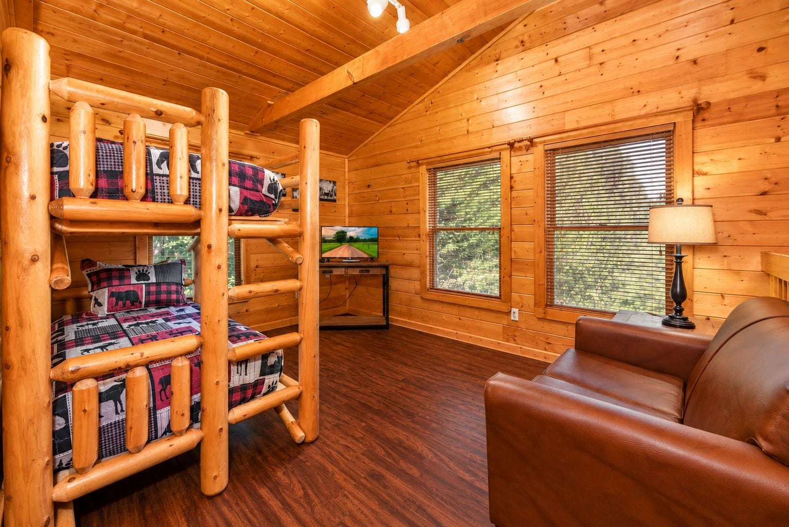 A cabin interior with a bunk bed, a television, a leather sofa, and wooden walls.