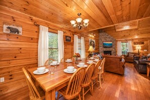 A wooden cabin interior with a dining area, living room, and fireplace.