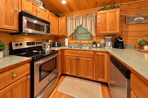 A kitchen with wooden cabinets, stainless steel appliances, a window with a green trellis, and a countertop with a coffee maker and toaster. - ❤Family Friendly❤3 Min to Parkway❤Gameroom, Hot Tub, Theater❤ (Pigeon Forge)